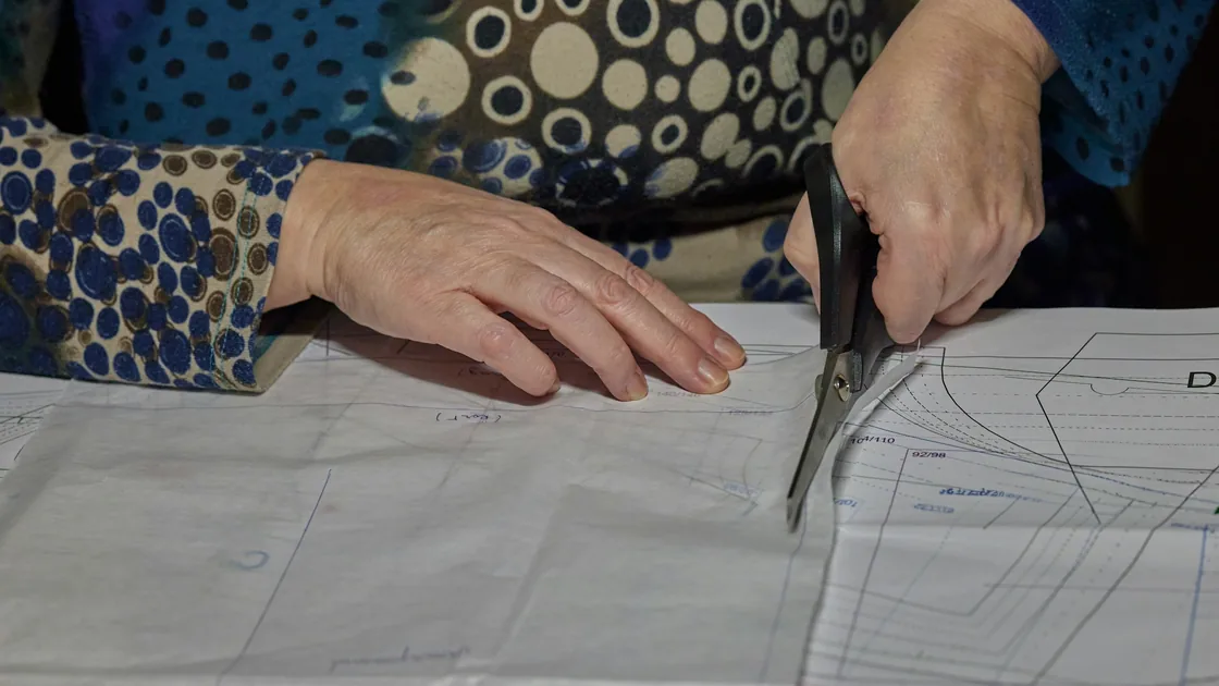 Manos recortando con tijeras un patrón de papel sobre la mesa de corte de un taller de costura